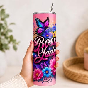 A hand holds a pink boss tumbler wrap featuring a vibrant floral butterfly rainbow design with a shiny straw.