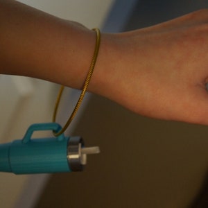 May include: A turquoise blue thermos with a gold chain attached to a person's wrist.