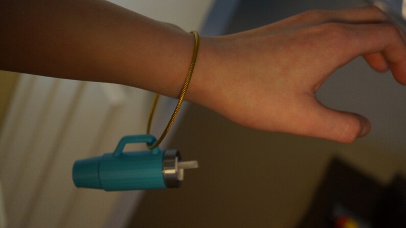 May include: A turquoise blue thermos with a gold chain attached to a person's wrist.