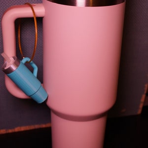 May include: A pink stainless steel travel mug with a white lid and a straw. The mug has a handle and a small blue object attached to it.
