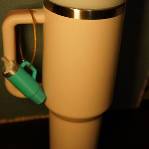 May include: A light pink travel mug with a silver lid and a straw sticking out of the lid. A teal blue keychain is attached to the handle.