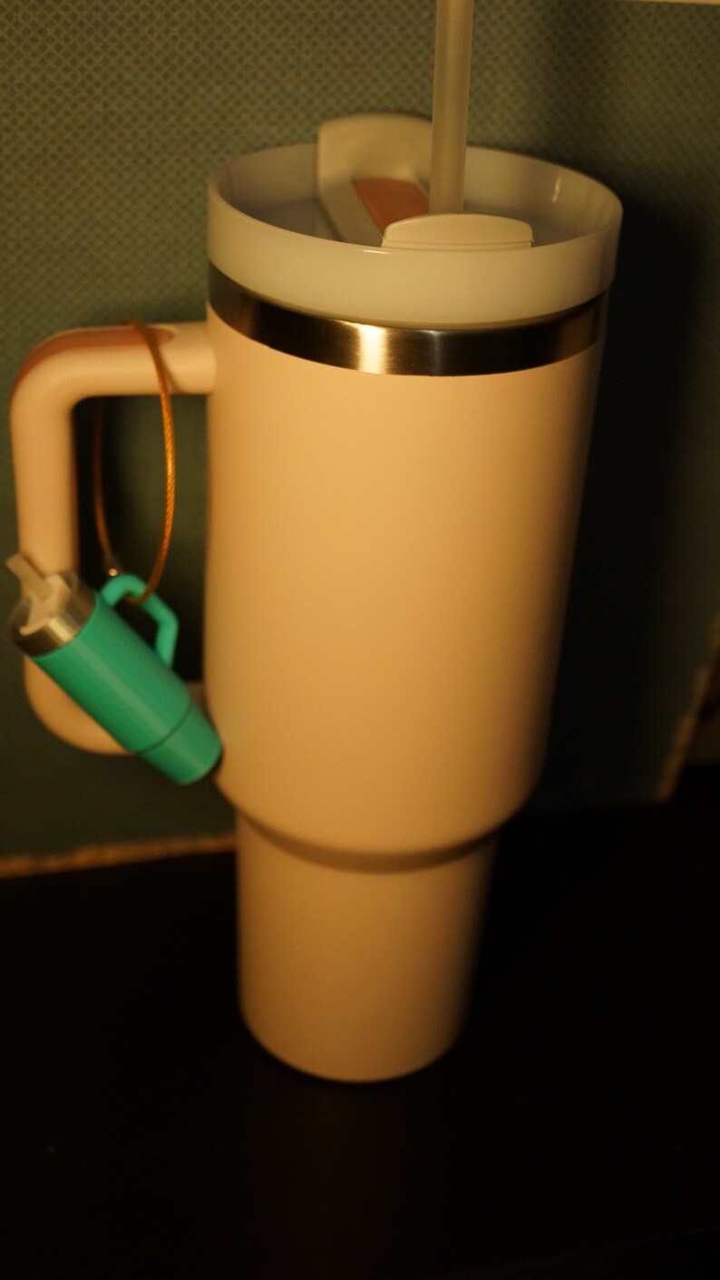 May include: A light pink travel mug with a silver lid and a straw sticking out of the lid. A teal blue keychain is attached to the handle.