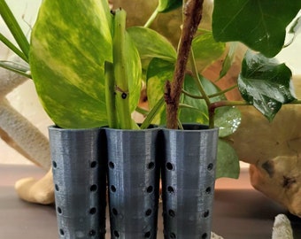 May include: Three black plastic plant supports with holes for drainage. The supports are in a row and are used to help plants grow upright.