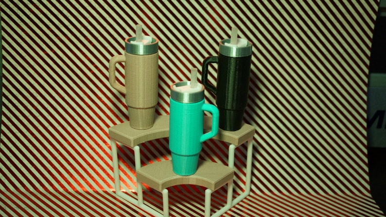 May include: Three travel mugs with lids and straws, displayed on a tiered stand. The mugs are beige, black, and turquoise.