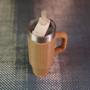 May include: A brown travel mug with a stainless steel lid and a white plastic straw holder. The mug has a handle and a textured exterior.