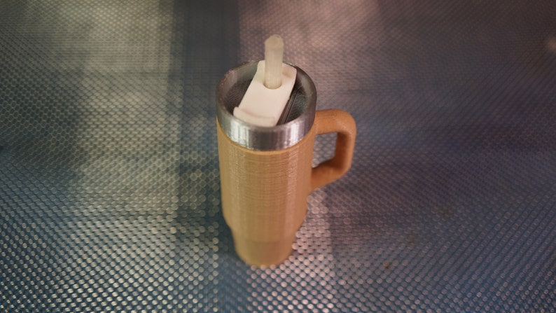 May include: A brown travel mug with a stainless steel lid and a white plastic straw holder. The mug has a handle and a textured exterior.