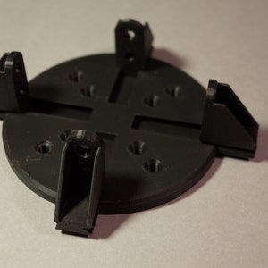 以下が含まれることがあります： 黒いプラスチック製のベースと4本の調節可能なアーム。ベースは円形で、縁の周りに複数の穴があります。アームはベースに取り付けられており、さまざまな角度に調整できます。