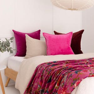 May include: A bed with a floral throw and several cushions. The cushions are in shades of pink, burgundy, and beige. The throw has a pink background with a colourful floral design. A white paper lantern hangs from the ceiling.