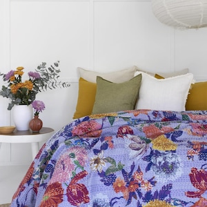 Peut inclure: Un lit avec une couverture à motifs floraux dans les tons de violet, rose, jaune et rouge. La couverture est ornée de détails cousus. Le lit est décoré de divers coussins blancs, verts et jaunes. Un vase de fleurs est posé sur une table de chevet.