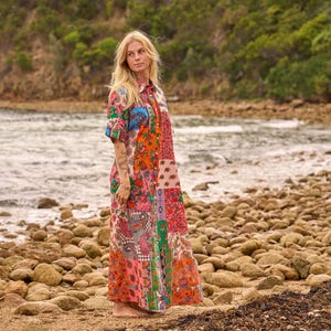 May include: A long-sleeved maxi dress featuring a vibrant patchwork design with various floral and paisley patterns in shades of orange, pink, green, and blue. The dress has a button-down front, a classic collar, and a loose, flowing silhouette.