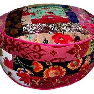 Könnte beinhalten: Ein runder Patchwork-Pouf mit einer Mischung aus Blumen- und Paisley-Mustern in Rot-, Rosa- und Grüntönen. Der Pouf hat eine leuchtend rosa Umrandung und ein weiches, strukturiertes Aussehen, perfekt, um jedem Raum einen Farbtupfer zu verleihen.