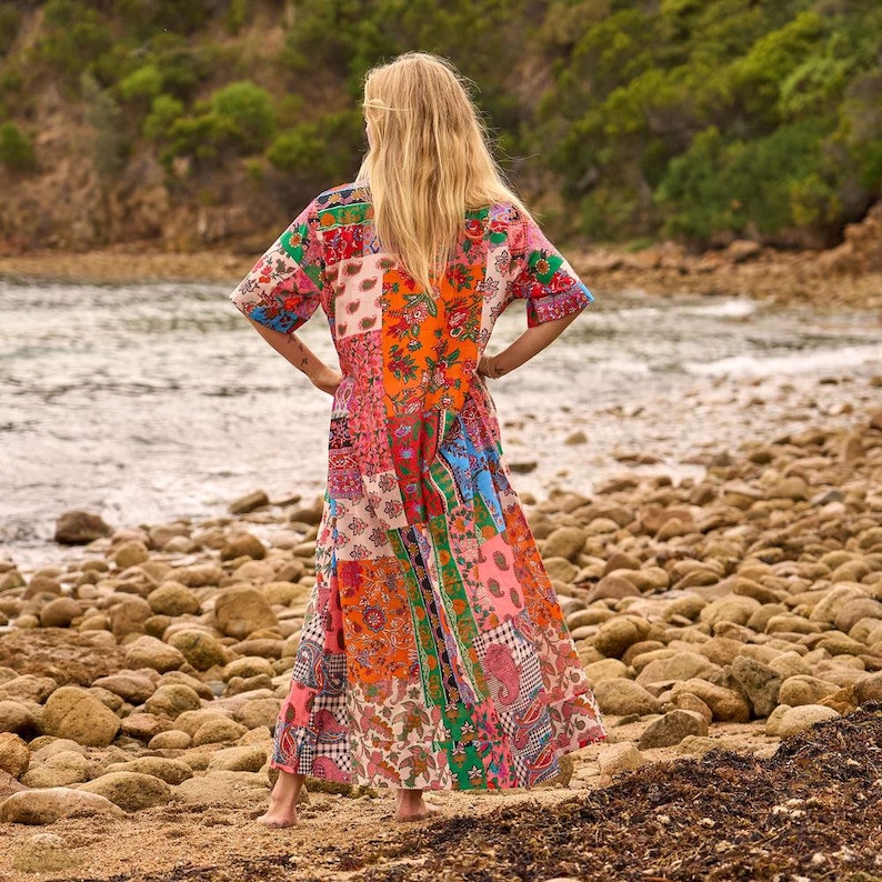 Puede incluir: Un vestido largo hasta los pies con un dise&ntilde;o de patchwork vibrante que presenta varios estampados florales y de cachemira en tonos naranja, rosa, azul, verde y blanco. La prenda tiene mangas cortas y una silueta holgada y fluida hasta los tobillos.