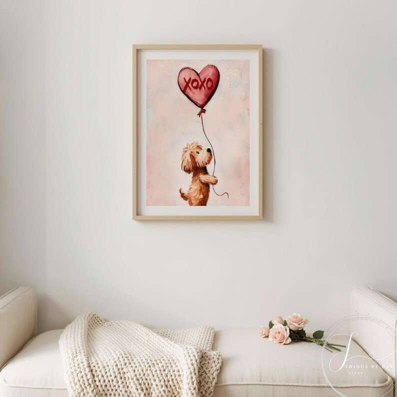 May include: A framed print with a watercolour illustration of a dog holding a heart-shaped balloon. The red balloon has the text "XOXO" on it. The artwork has a soft, pink background and is in a light wood frame.