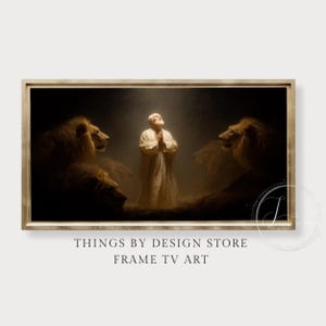 May include: Framed artwork showing a man in white robes praying, lit by a shaft of light, flanked by two lions in a dark setting. The text "THINGS BY DESIGN STORE FRAME TV ART" is at the bottom of the image.