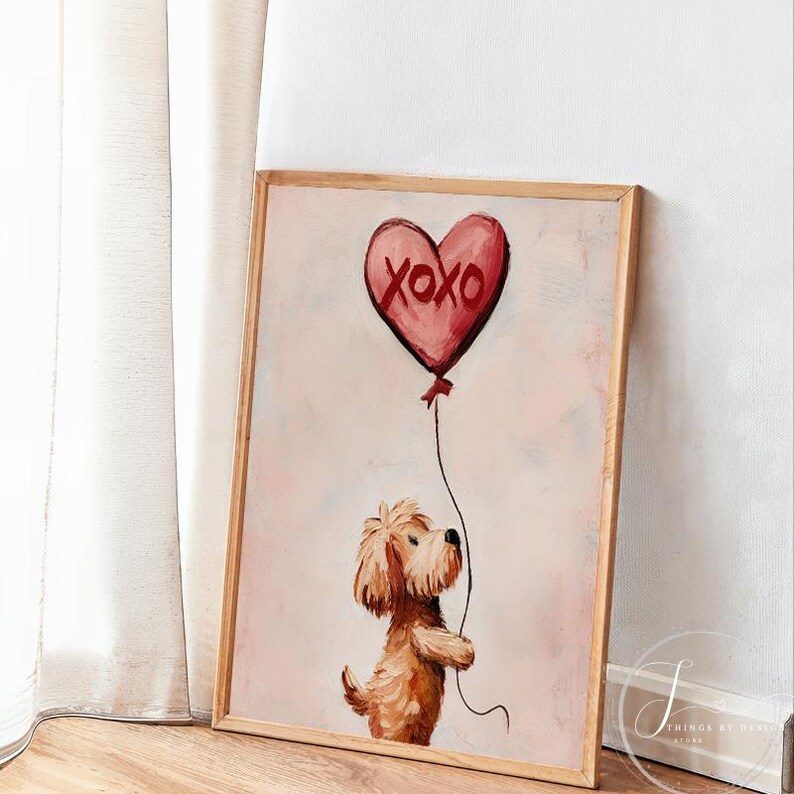 May include: A framed painting featuring a brown dog holding a red heart-shaped balloon with the text "XOXO". The artwork has a light pink background and a wooden frame. The dog is painted in a whimsical style.
