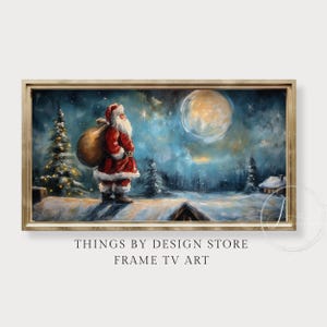 May include: A framed digital art print depicts Santa Claus with a sack, standing in a snowy landscape under a full moon. The artwork features a color palette of blues, whites, and reds, with a gold-colored frame. Text at the bottom reads "THINGS BY DESIGN STORE FRAME TV ART."