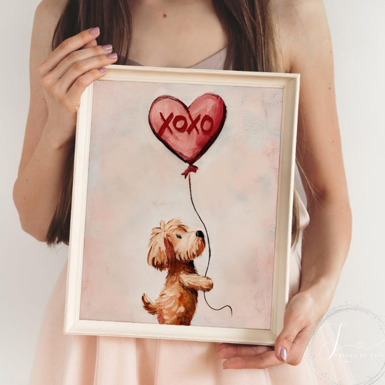 May include: A framed print showing a brown dog holding a red heart-shaped balloon with "XOXO" on it. The artwork has a soft, painterly style with a light pink background. The image is in a white frame.