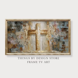 May include: A framed rectangular artwork featuring a textured, abstract painting of a cross. The cross is centrally positioned, with a light brown and white colour palette. The background has shades of blue, brown, and beige. The text "THINGS BY DESIGN STORE FRAME TV ART" is at the bottom.
