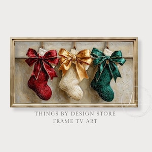 May include: A framed artwork featuring three Christmas stockings. The stockings are red, gold, and green, each adorned with a matching bow. The artwork has a textured, painted appearance, with a neutral background and a gold-colored frame.