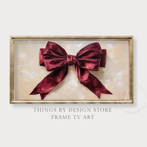 May include: A framed artwork depicting a large, deep red bow on a textured, cream-coloured background. The bow is rendered with detailed shading, and the frame is a light gold colour. The text at the bottom reads "THINGS BY DESIGN STORE FRAME TV ART."