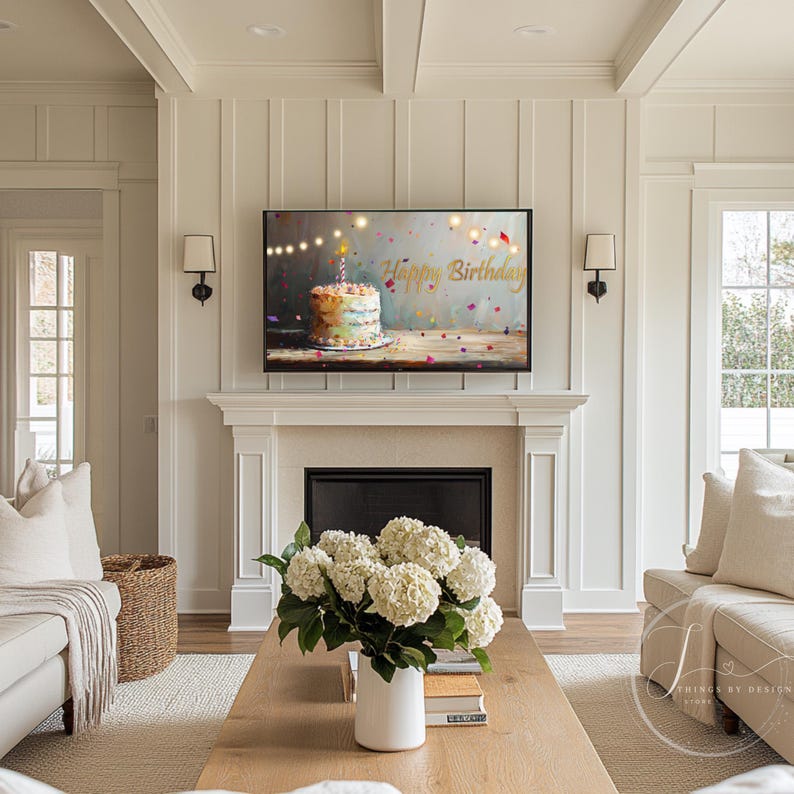 May include: A white living room with a fireplace and a television playing a birthday cake with the words "Happy Birthday" on the screen. There is a bouquet of white flowers on a wooden coffee table.