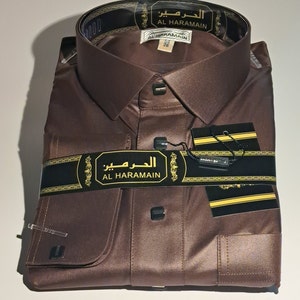 May include: A brown long-sleeved shirt with a button-down collar and a pocket on the left side. The shirt has a black label with the text "الهرم" (Al Haramain) on it.