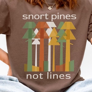 May include: Espresso-colored t-shirt with the text "snort pines not lines" above a graphic of stylized trees in green, orange, and yellow. The shirt is a Comfort Colors 1717 style.