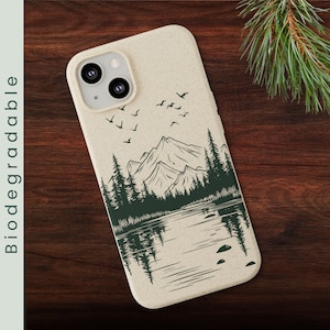 May include: A beige phone case with a black and white illustration of a mountain range, a lake, and trees. The case has a cutout for a camera lens and a biodegradable label.