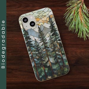 May include: A phone case with a stained glass design of a forest scene. The case features a blue, green, and brown color scheme with a variety of trees and mountains. The case has a clear back and a white border.