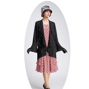 May include: A woman wearing a black dress with a red and white pattern, a black cardigan with ruffled sleeves, a black hat with a white ribbon, and black shoes.
