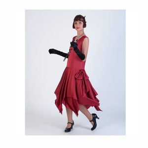 May include: A woman in a red flapper dress with a black bow at the waist. She is wearing black gloves and black shoes. She has short, dark hair and is wearing a headband.