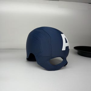 May include: A navy blue Captain America helmet with a white "A" on the side. The helmet has a textured surface and a chin guard. The superhero helmet is a replica of the one worn by Captain America.