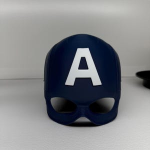 May include: A navy blue Captain America mask with a white "A" emblem. The mask has eye openings and a textured surface. This superhero-themed accessory is likely for cosplay or costume use.