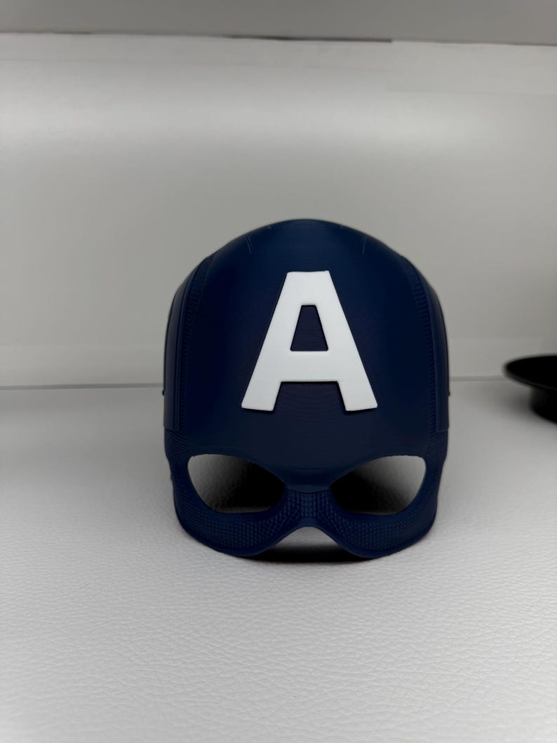 May include: A navy blue Captain America mask with a white "A" emblem. The mask has eye openings and a textured surface. This superhero-themed accessory is likely for cosplay or costume use.