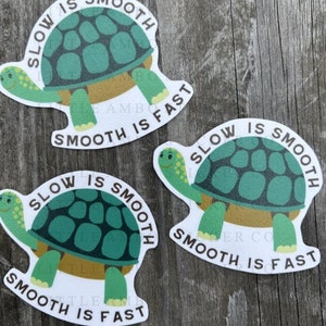 May include: Three turtle stickers with the text "Slow is Smooth, Smooth is Fast". Each sticker features a green turtle with a brown shell and a white border. The stickers are on a wooden surface.