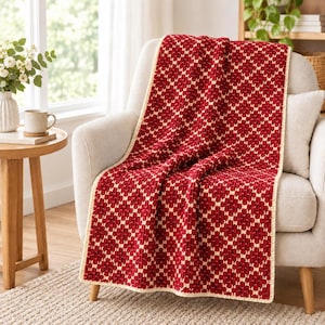 May include: A rectangular crochet blanket featuring a repeating diamond pattern in deep red and cream yarn. The blanket has a textured surface with a cream-colored border and is draped over a light-colored upholstered armchair.