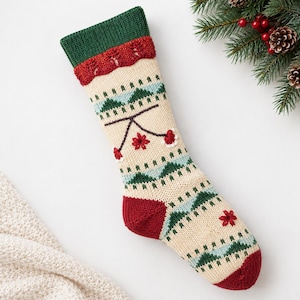 Könnte beinhalten: Ein cremefarbener Strick-Weihnachtsstrumpf mit dunkelgrünem Bündchen, einem roten strukturierten Band und einem wiederkehrenden Muster aus grünen und hellblauen geometrischen Formen. Das Design enthält kleine rote Blumenakzente sowie eine rote Ferse.