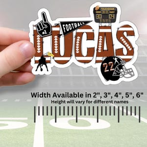 May include: Brown and white football-themed name decal with the name "LUCAS" in a brown and white striped font. The decal includes a football, a whistle, a football player, a football helmet, and a scoreboard. The decal is available in sizes 2 inches, 3 inches, 4 inches, 5 inches, and 6 inches.