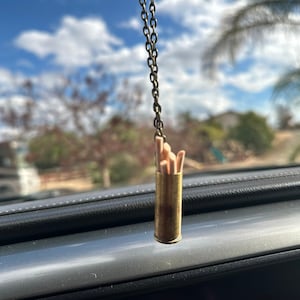 May include: A gold chain hangs from a rearview mirror with a brass bullet casing filled with wooden matches.