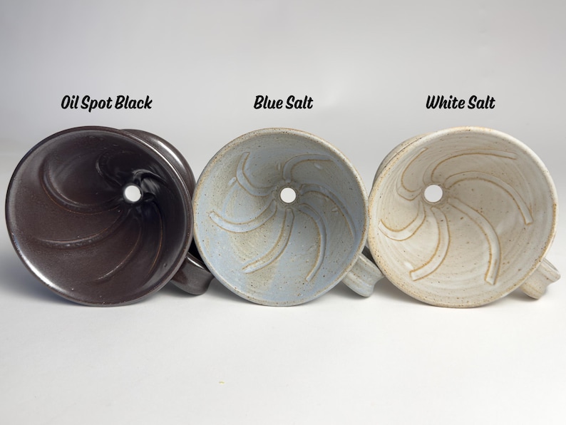 May include: Three ceramic pour-over coffee makers in Oil Spot Black, Blue Salt, and White Salt. Each has a central hole and a handle. The names of the colors are written above each coffee maker.
