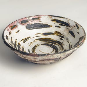 May include: A white ceramic bowl with a black and brown swirl design. The bowl has a slightly uneven rim and a rustic appearance.
