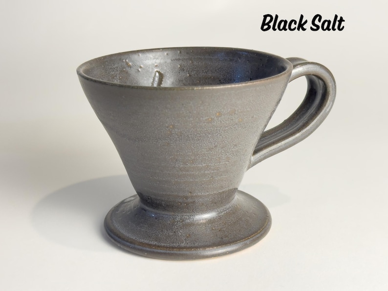 May include: A handmade, dark gray ceramic pour-over coffee maker with a handle and a wide base. The words "Black Salt" are written in black script at the top right.