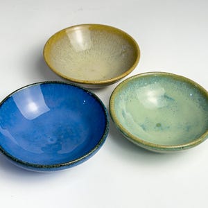 May include: Three small ceramic bowls in different colors. The bowls are blue, green, and yellow with a speckled glaze.