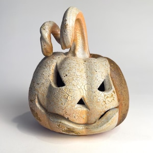 May include: A ceramic jack-o'-lantern sculpture featuring a white crackle glaze finish with orange and brown undertones. The pumpkin has a carved face with triangular eyes and a wide, curved mouth, topped with a curved, textured stem.
