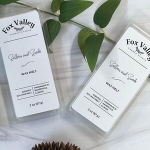 May include: Two clear plastic clamshell containers of Saffron and Suede scented soy wax melts from Fox Valley Candle Studio. Each white label features the brand name, scent, and the text Handmade in Naperville, Illinois, with a weight of 2 oz (57 g).