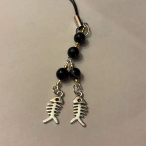 May include: Black and gold beaded phone charm with two silver fishbone charms.