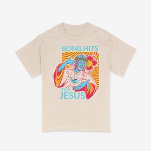 Könnte beinhalten: Ein beiges T-Shirt mit einem Grafikdruck von Jesus, der eine Bong hält, und dem Text "Bong Hits For Jesus" im Retro-Stil.
