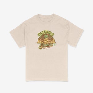 May include: A beige t-shirt featuring a vintage-style graphic of a pineapple, palm trees, and a train with the text "Pineapple Express" and "Sativa Blend 15% THC".