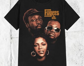 May include: A black short-sleeve t-shirt featuring a graphic print of the musical group Fugees. The design includes portraits of the three members and the text Fugees The Score in a tan color. The shirt has a crew neckline and a straight hem.