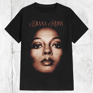 K&ouml;nnte beinhalten: Schwarzes T-Shirt mit einem Sepia-farbenen Bild von Diana Ross. Der Text "DIANA ROSS" befindet sich in einer kursiven Schriftart &uuml;ber dem Bild. Das T-Shirt hat einen Rundhalsausschnitt und kurze &Auml;rmel.